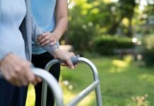 Family caregivers feeling squeezed in Washington, report finds Image of an unrecognizable senior woman being assisted to walk using a walker by caregiver at park.