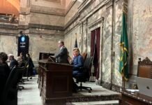 Longtime Mariners broadcaster Rick Rizzs waves to the Capitol press corps on the Washington state Senate floor as the team is honored Monday, Feb. 2, 2026