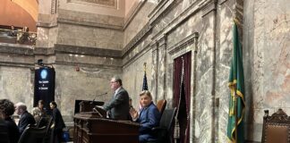 Longtime Mariners broadcaster Rick Rizzs waves to the Capitol press corps on the Washington state Senate floor as the team is honored Monday, Feb. 2, 2026