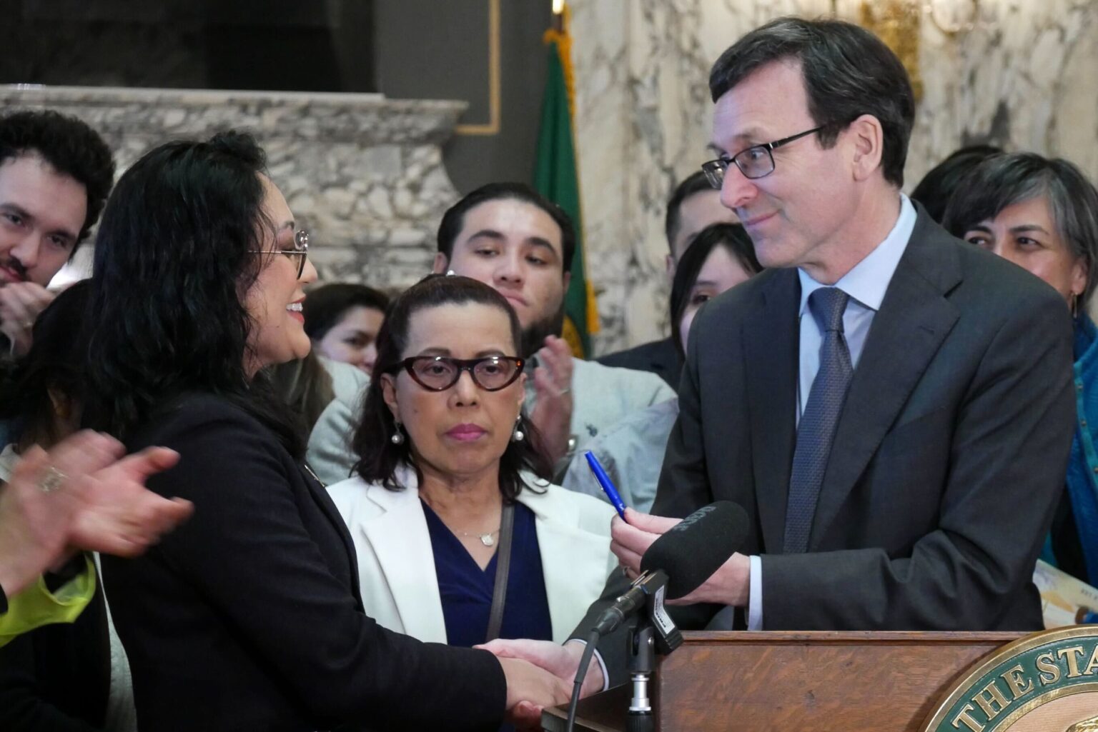 Washington Gov. Bob Ferguson hands Democratic state Sen. Yasmin Trudeau the pen he used to sign Trudeau’s bill to regulate automated license plate readers. The bill was signed into law on March 30, 2026 in Olympia. (Photo by Aspen Ford/Washington State Standard)