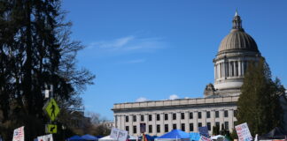 Protesters lined the street near the Washington state capitol campus waving political signs on March 28, 2026.