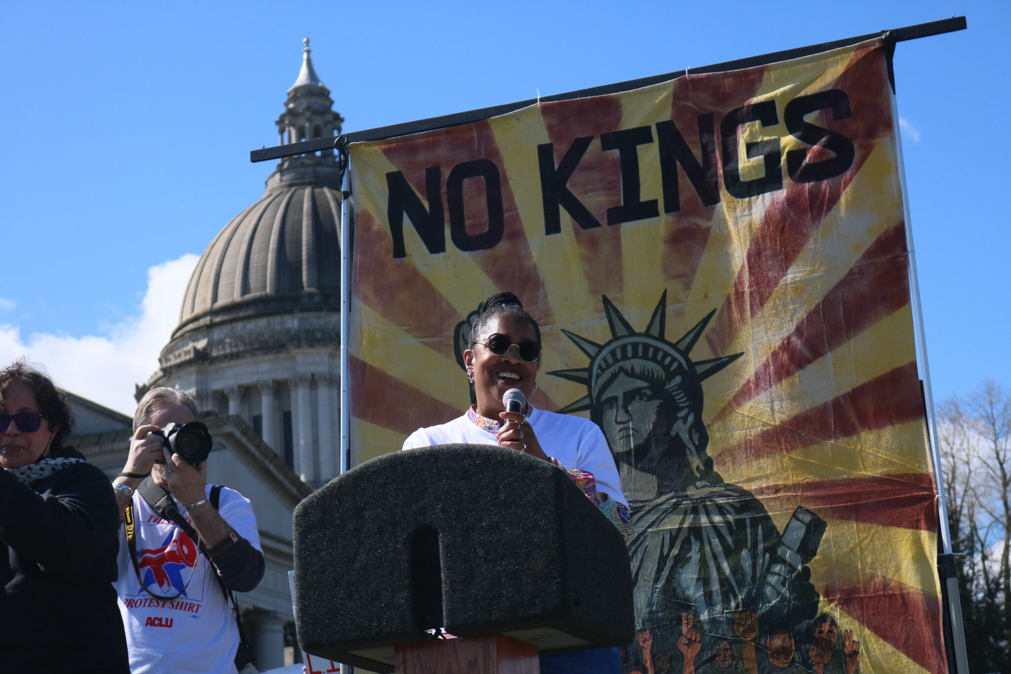 Michele Storms, executive director of the Washington state American Civil Liberties Union, speaks to a crowd during the No Kings protest on Saturday March 28, 2026. (Aspen Ford/Washington State Standard)