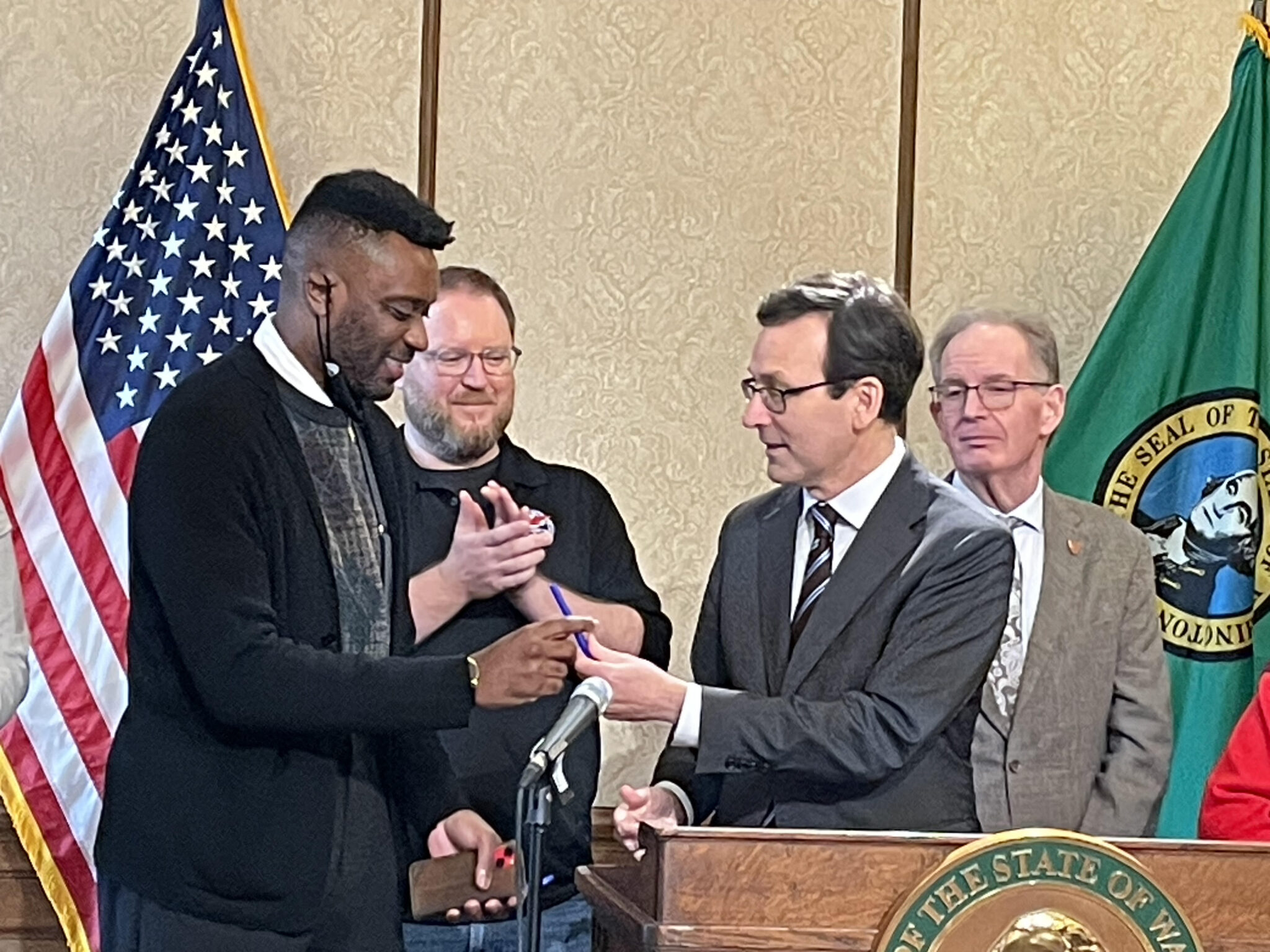 Washington Gov. Bob Ferguson hands Democratic state Rep. Shaun Scott the pen that the governor used to sign Scott’s bill to increase funding for wildfire mitigation. The bill was signed into law on March 23, 2026 in Olympia, WA. (Photo by Jerry Cornfield/ Washington State Standard)