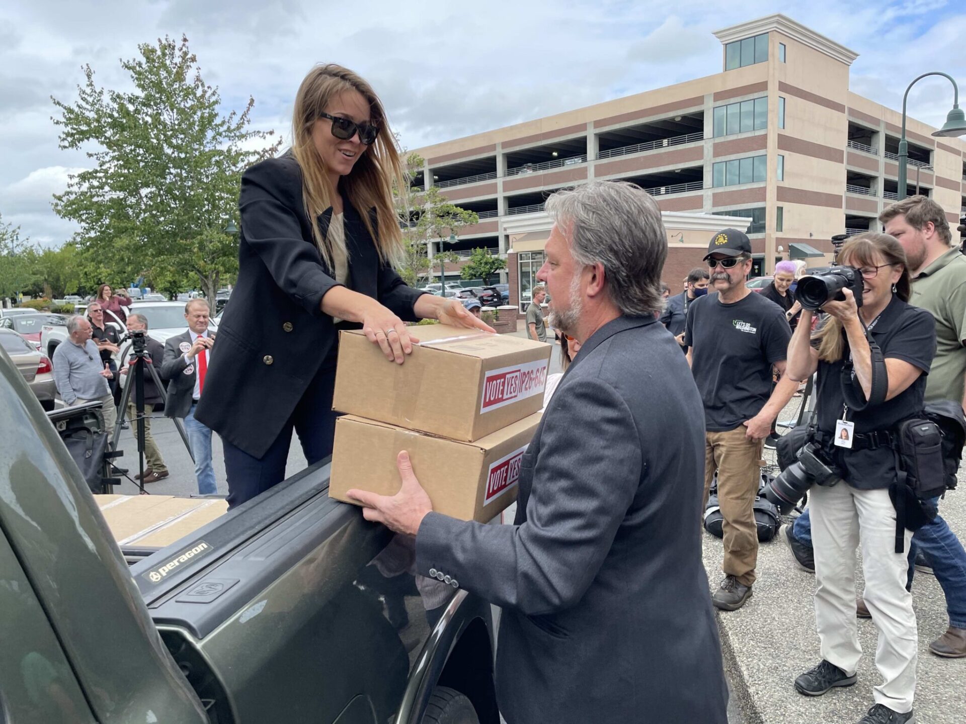 Ashley Butenschoen, a volunteer for Let’s Go Washington, hands boxes of ballot initiative petitions to the group’s founder, Brian Heywood, on Thursday, July 2, 2026, at the secretary of state’s office in Tumwater.